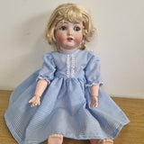 Doll wearing a blue checkered dress on a wooden surface