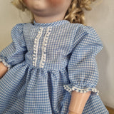 Close-up of a blue checkered dress with white trim on a neutral background