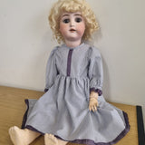 Vintage doll with blonde hair and a striped dress on a white surface.