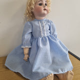 Doll wearing a blue checkered dress on a wooden surface