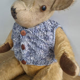 Stuffed animal wearing a knitted blue sweater with brown buttons on a light gray background